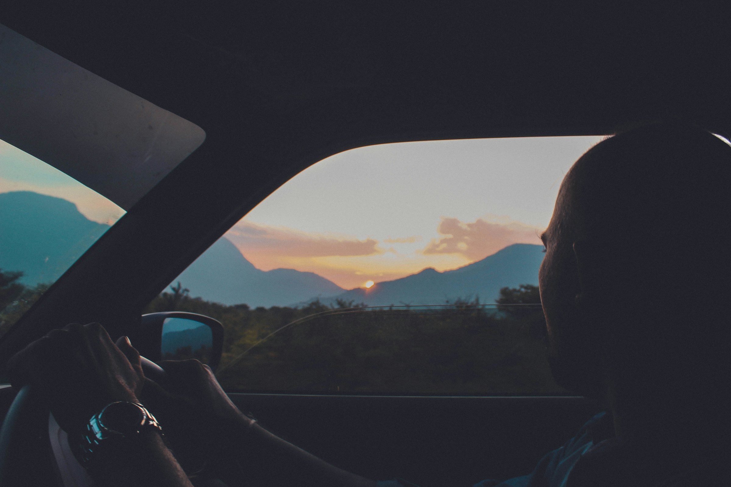 Conductor de espaldas manejando hacia el atardecer